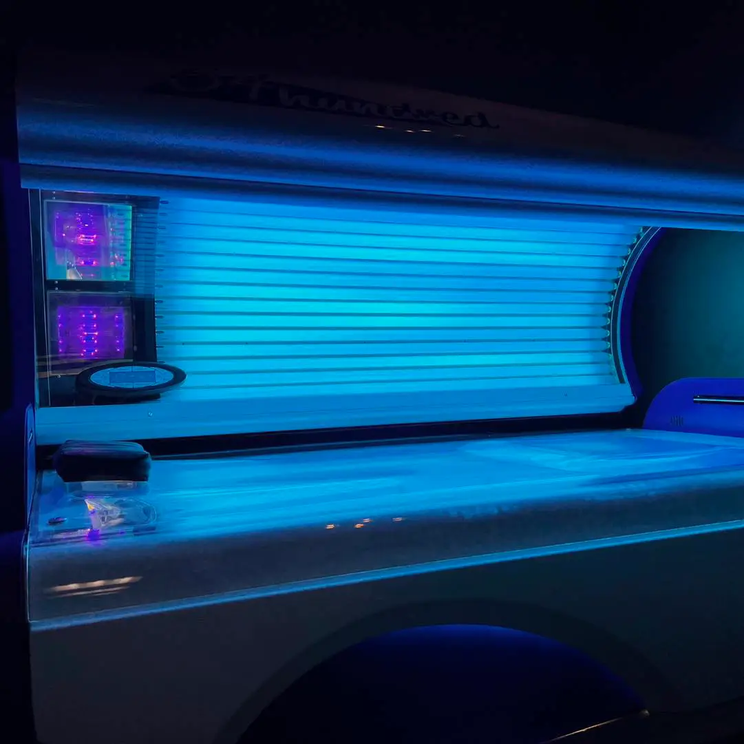An open, empty UVA tanning bed at Ultra Tan at First Impressions glowing with bright blue light in a dark room.